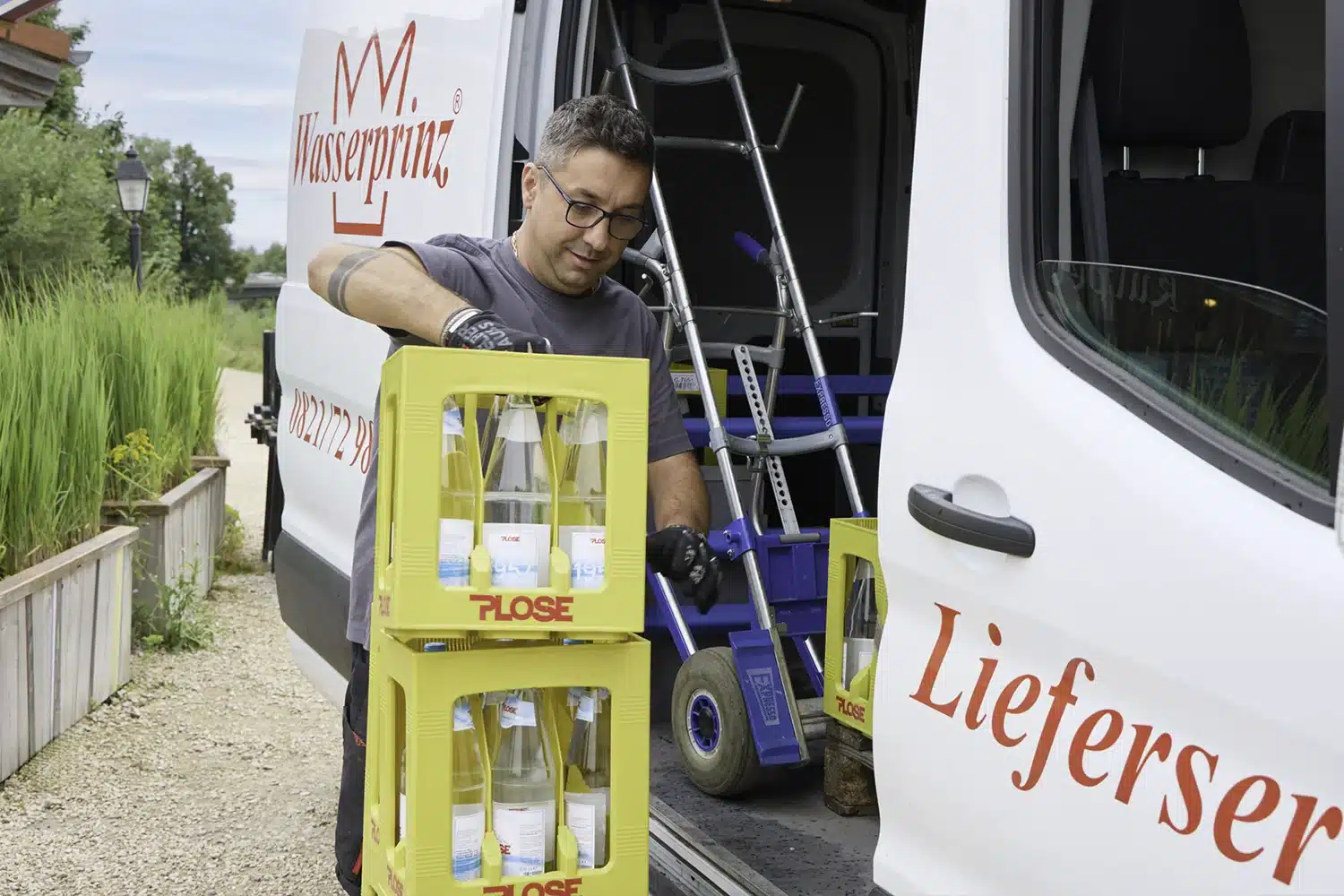 Wasserprinz-Mitarbeiter liefert Plose-Mineralwasser und Getränkekisten per Sackkarre aus dem Lieferwagen – Getränkelieferservice Augsburg