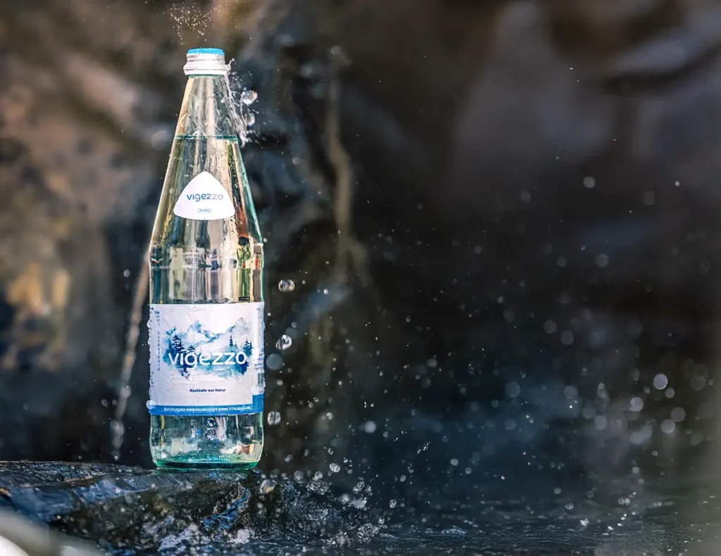 Flasche vigezzo Wasser steht auf einem Stein und wird von Quellwasser beregnet