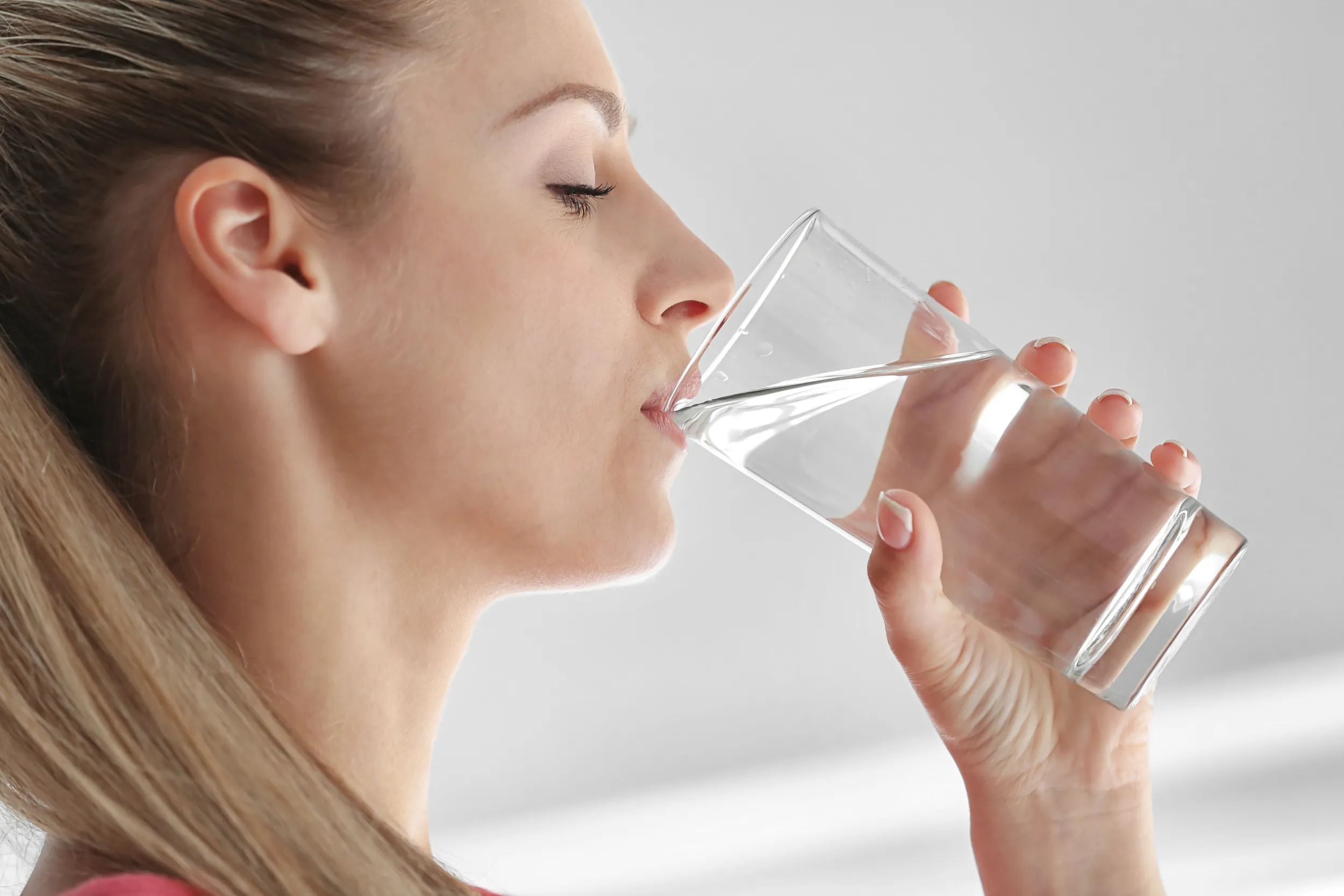 Junge Frau trinkt genug Wasser aus einem Glas.