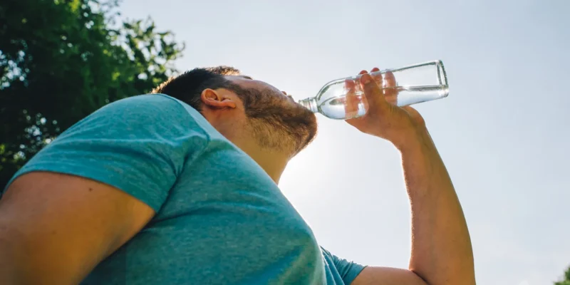 Mann trinkt viel aus einer Glasflasche Wasser