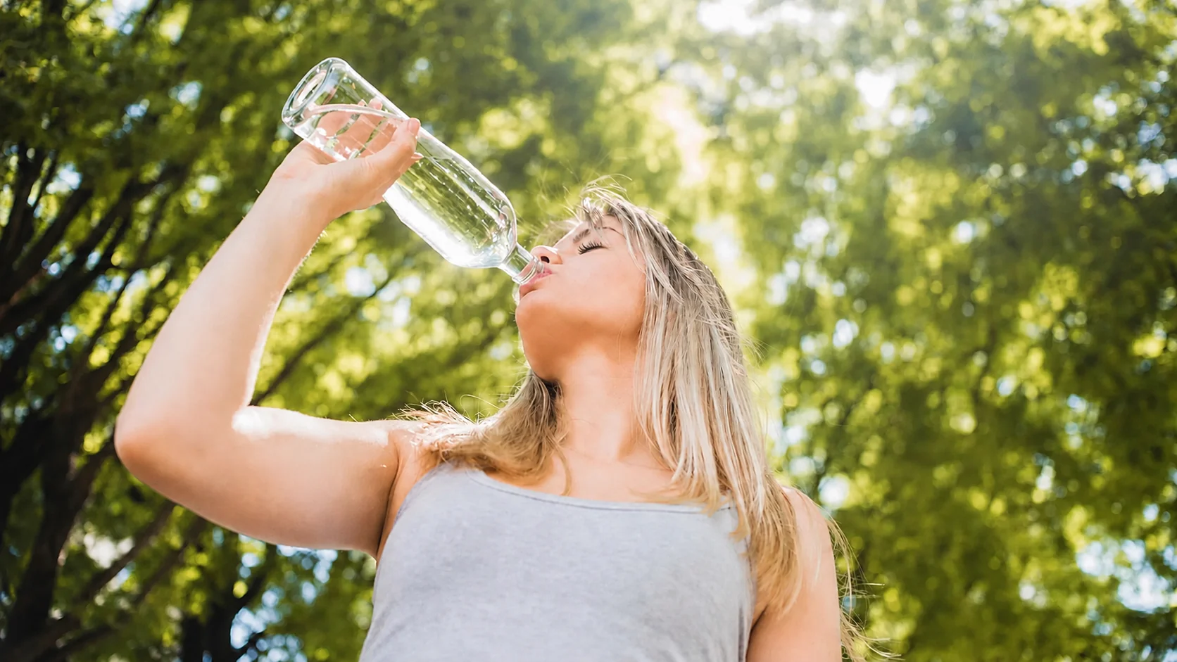 Frau trinkt aus Wasserflasche viel Wasser um nicht zu dehydrieren