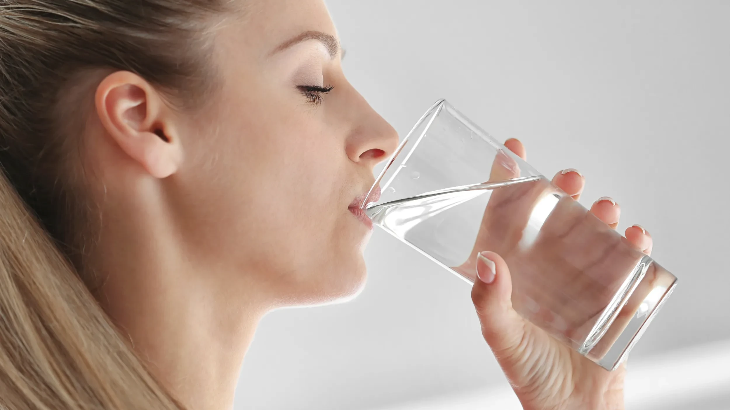 Junge Frau trinkt genug Wasser aus einem Glas.